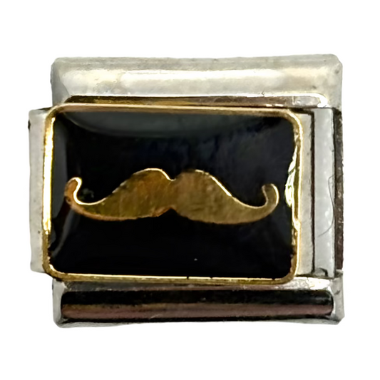 Silver charm with a black background and gold mustache design on a white background